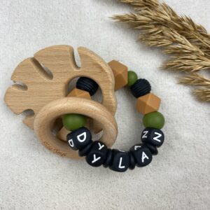 Bijtring met naam, zwarte letters en een houten blaadje en ring.